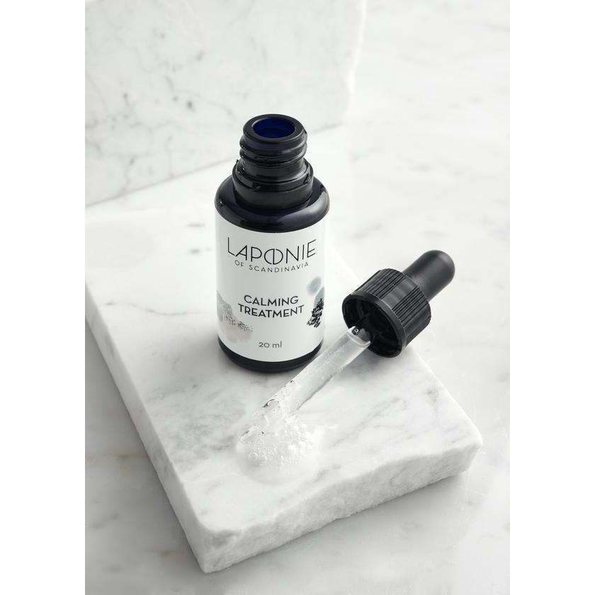 A bottle of Laponie of Scandinavia Calming Treatment Serum for sensitive skin rests on a white marble slab, with hydrating gel-serum visible in the dropper.