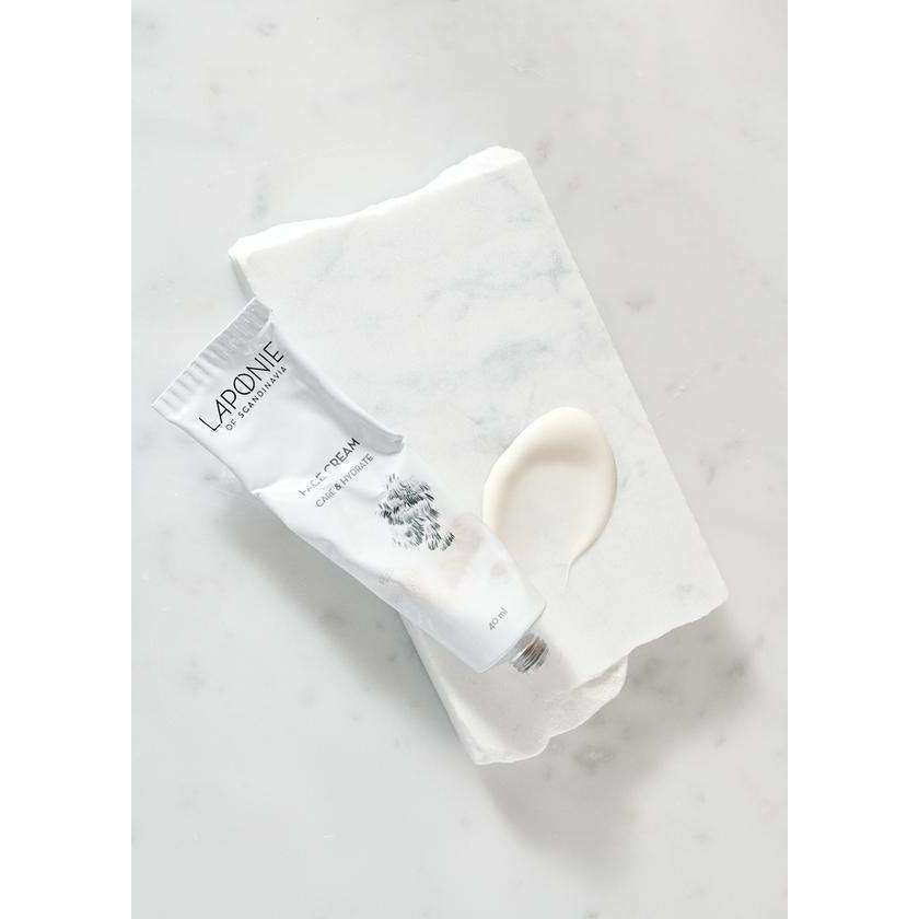 A white tube of Laponie of Scandinavia Face Cream rests on parchment beside a dab of cream, all atop light marble—a gentle formula by Laponie of Scandinavia for sensitive skin.