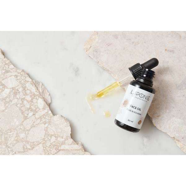 A bottle of Laponie of Scandinavia Face Oil with a dropper, made for sensitive skin, rests on a marble surface with some spilled oil. Light stone textures appear in the background.