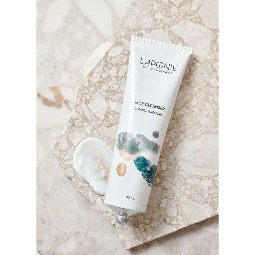 A tube of Laponie of Scandinavia Milk Cleanser rests on marble, with a dab of the gentle formula beside it. The 100 ml tube displays abstract art and text noting it's a cleanser for sensitive skin by Laponie of Scandinavia.