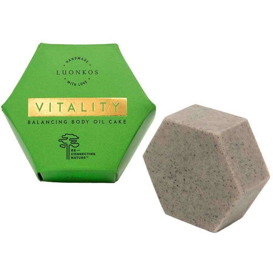 The Luonkos Vitality Body Oil Cake comes in a hexagonal green box with a tree logo, alongside a speckled gray bar. Enriched with Forest Microbe Extract, it supports your skin microbiome. Packaging features the Luonkos brand name.