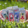 A basket with a red-and-white checkered cloth displays several Nordqvist Moomin Sweetheart tea packages—featuring Moomin characters and black tea with wild strawberry—outdoors on green grass in bright sunlight.