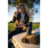 A woman sits on a car hood enjoying Renjer Nordic Elk Jerky Black Pepper, savoring its smoky taste and hint of black pepper.