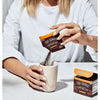 A person pours Four Sigmatic Instant Mushroom Coffee Lions Mane powder from a packet into a marble mug, with the Four Sigmatic product box visible on the table.