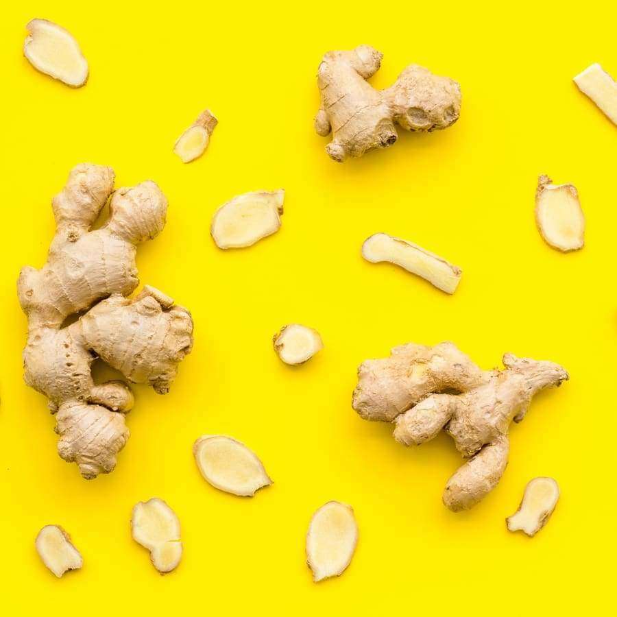 Whole ginger roots and slices are scattered on a bright yellow background, evoking ingredients found in Havuka Cabbage-Ginger-Spruce Resin Balm by Havuka for natural osteoarthritis pain relief.