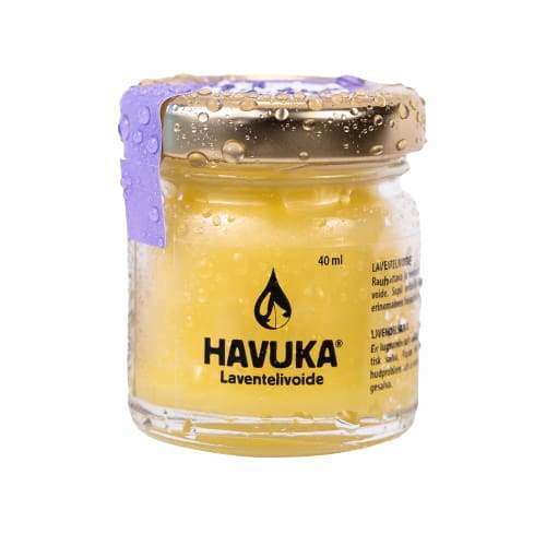 A small glass jar of Havuka Lavender Balm with a gold lid is covered in water droplets. The yellow cream inside, marked with the Havuka logo, offers gentle eczema relief with each application.