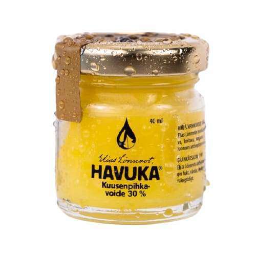 A small glass jar with a gold lid, labeled Havuka Strong 30% Spruce Resin Balm, contains a yellow balm valued for its natural antiseptic and wound healing properties. The water-covered jar is by the brand Havuka.