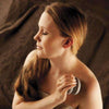 A woman with long brown hair wrapped in a towel gently exfoliates her shoulder using the Hukka Sauna-Joy Massage Aid by Hukka against a soft brown fabric background, creating a soothing moment of self-care.