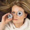 A woman with long blonde hair and a calm expression wears a white sweater while playfully holding Hukka Orbits Eye Stones from Hukka over her eyes like glasses.