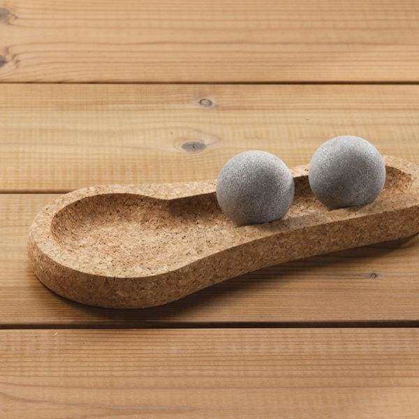 Two smooth, gray Hukka Solejoy massage balls by Hukka sit on a footprint-shaped cork base, displayed on a wooden surface.