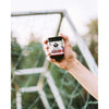 A hand holds a small jar labeled “Puhdistamo Electrolyte Powder Forest Fruit” by Puhdistamo in front of a soccer goal net outdoors, suggesting its support for hydration, with the background softly blurred.