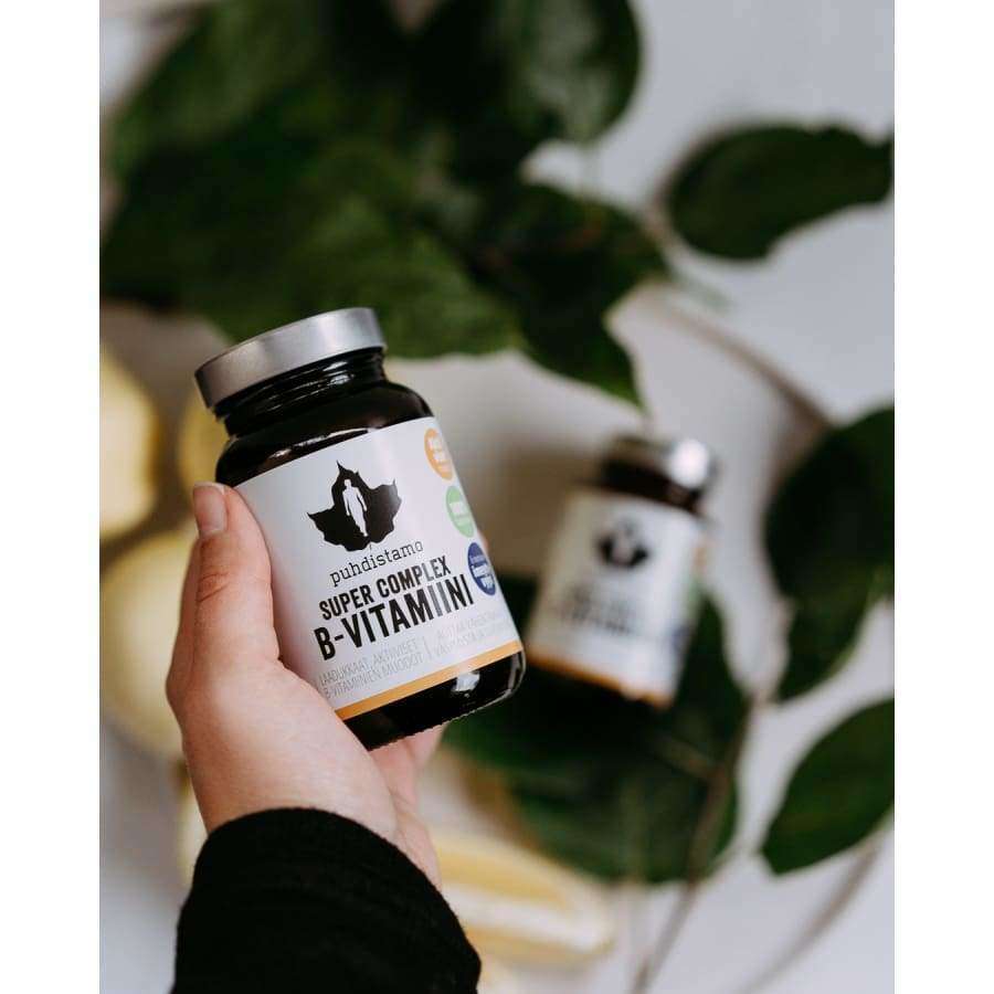 A hand holds a bottle of Puhdistamo Super Complex B-complex, a highly absorbable vitamin B supplement by Puhdistamo, with another bottle and green leaves blurred in the background.
