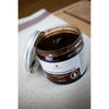 An open Emendo Sauna Peat Mask jar with a silver lid rests on a textured light surface—ideal for face and body care, featuring authentic Finnish peat by Emendo.